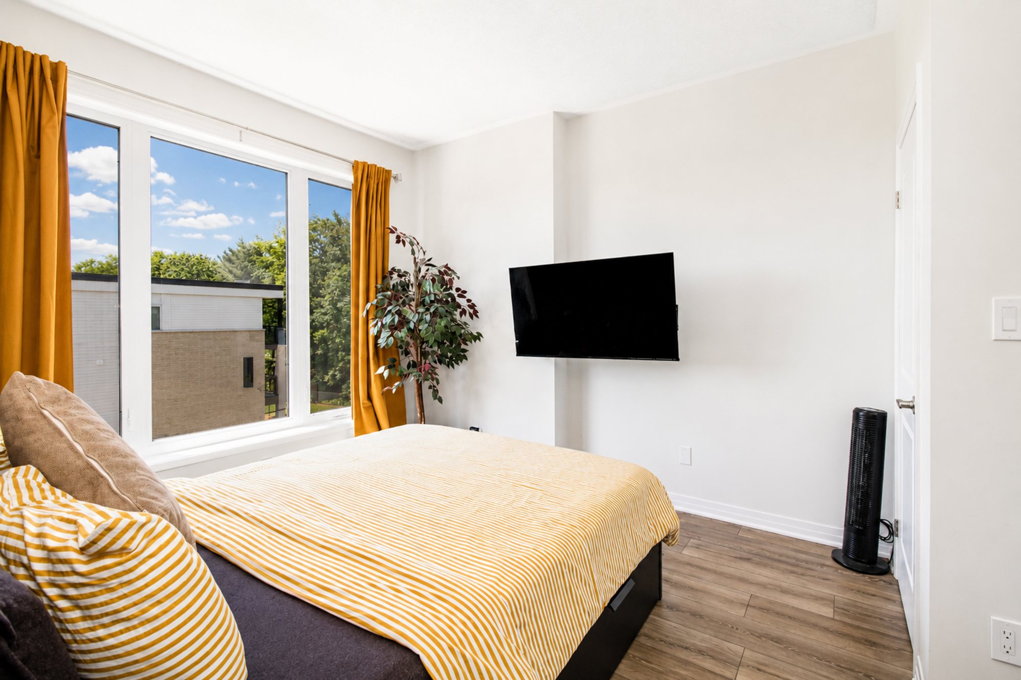 Bright bedroom with warm accents, a leafy view and wall-mounted TV